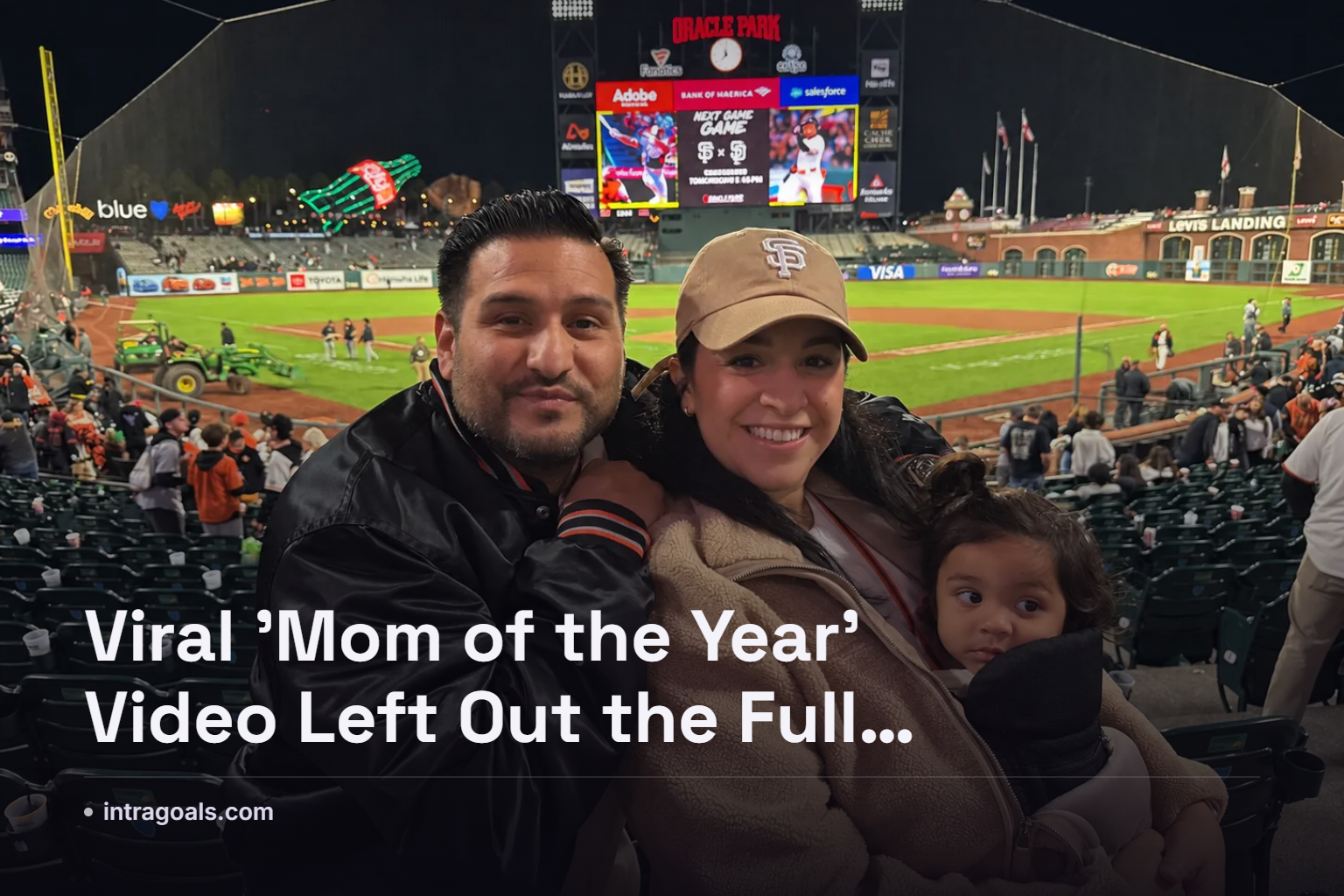 Parent holding a toddler and a tray of ballpark snacks while walking through stadium seating during a baseball game
